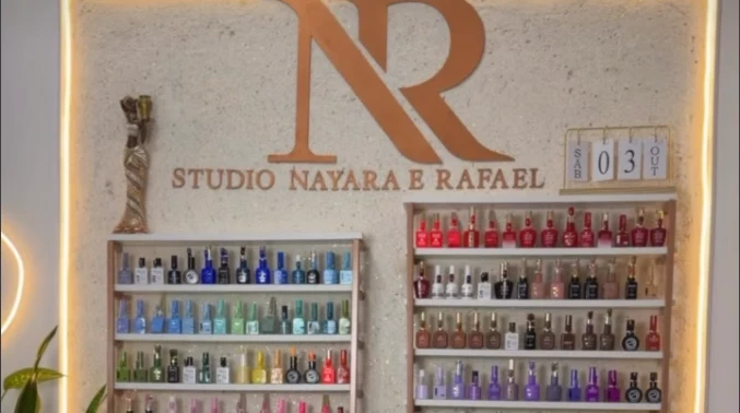 Parede do Studio Nayara & Rafael com o logotipo NR e prateleiras de esmaltes